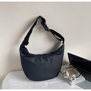 Close-up of black crescent crossbody bag with adjustable strap next to a laptop and headphones