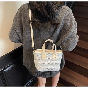 Detail of off-white straw bucket bag with hollow crochet texture and leather strap