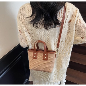 Detailed close-up of woven straw handbag with brown leather trim and gold metal rivets
