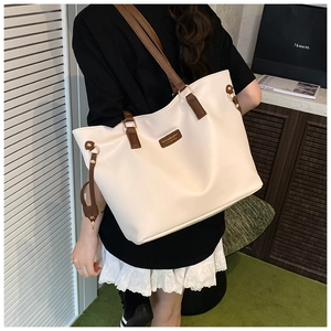 Detail of cream white PU leather tote bag featuring brown handles and branded leather patch