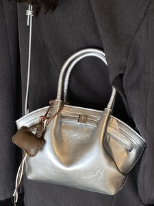 Silver metallic dumpling tote bag with dual handles and mini brown bag charm pendant