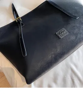 Gros plan d'un sac cabas noir avec boucle dorée et détail du logo de la marque embossé