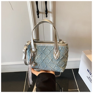 Detail of light blue denim handbag with quilted texture, silver trim and lace tassel