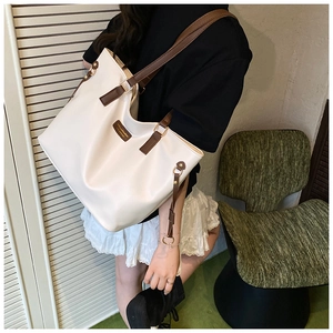 Close-up of cream tote bag with dark brown leather straps and brand patch detail