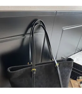 Détail d'un sac cabas noir en daim avec boucles dorées et texture mate élégante