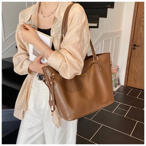 Detailed view of the large caramel brown tote bag worn on a woman's shoulder