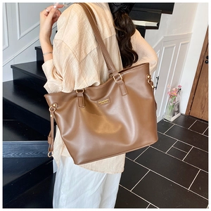 Close-up of a brown leather tote bag showing side drawstring detail and metal hardware