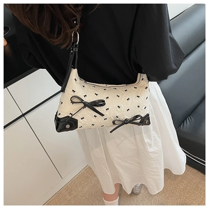 Detail view of cream handbag with black bows, showing pleat texture and zip closure
