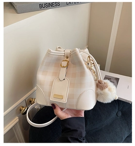 Detailed view of checkered bucket bag with magnetic closure and plush ball charm