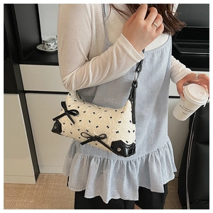 Detail of cream fabric shoulder bag featuring black bow embroidery and leather corner studs