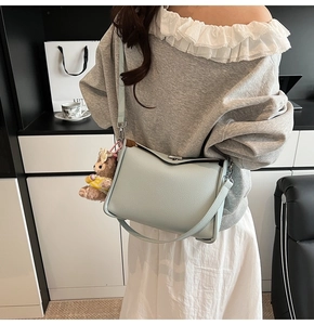 Detail of light blue litchi grain leather bag with a cute bear charm and thin strap