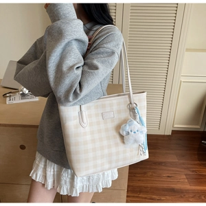 Detail of checkered tote bag with a blue bow plush pendant in a cozy interior setting