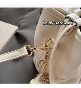 Detailaufnahme der karierten Beuteltasche mit goldener Hardware und Plüsch-Anhänger