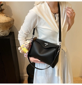 Detail of black lychee grain shoulder bag with silver turn-lock and plush bear charm