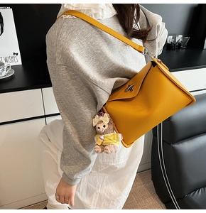 Detail of yellow litchi pattern leather crossbody bag with silver twist lock and plush charm