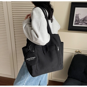 Detail of black canvas tote bag showing side hanging circular pouch with logo and multi-pockets