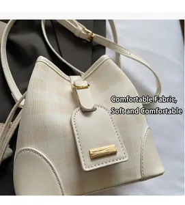Detail der cremefarbenen Beuteltasche mit gelbem Karostoff, Lederboden und Metallplakette
