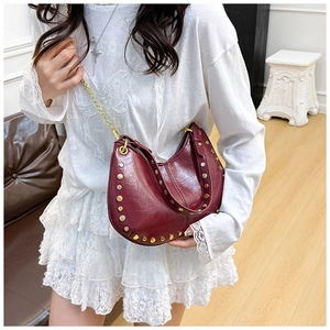 Detailed close-up of a burgundy leather crescent bag with golden studs and chain detail