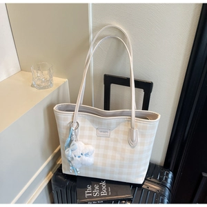 Close-up of beige checkerboard tote bag with plush doll charm on a suitcase