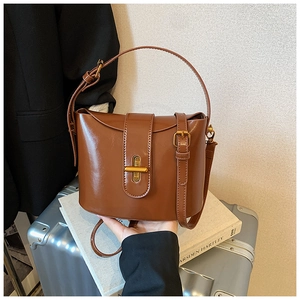 Detail einer karamellbraunen Beuteltasche mit goldenem Drehverschluss auf Gepäck
