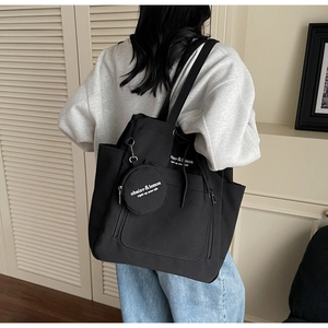 Detail of black canvas tote bag showing front pocket and mini round pouch attachment