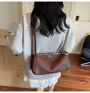 Brown pebbled leather shoulder bag with silver double zippers shown in a modern office
