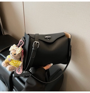 Close-up of black lychee leather bag featuring silver metal twist lock and cute bear charm