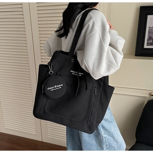 Detail view of black canvas tote bag with round coin purse and white printed logo on the strap