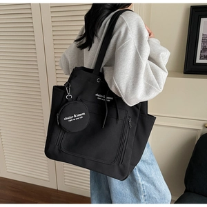 Detail view of large black canvas tote bag with a matching round coin purse on a shoulder
