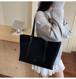 Gros plan du sac cabas noir mat montrant la boucle dorée et le logo discret embossé