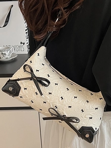 Elegant cream shoulder bag with black bow prints and rivet details on a model