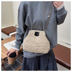 Détail d'un sac en paille beige avec chaîne dorée porté par un mannequin chic