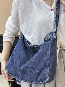 Sac hobo rétro en denim bleu foncé avec bords effilochés porté par un modèle au soleil