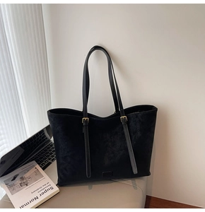 Détail de la texture d'un sac cabas en daim noir avec boucles dorées et bandoulière
