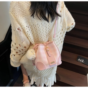 Detail of pink plaid bucket bag with plush charm and metal buckle on stairs