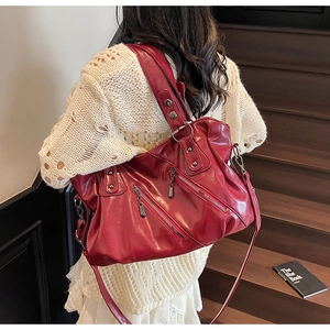 Dettaglio della borsa tote in pelle rossa con cerniere metalliche e borchie su modella