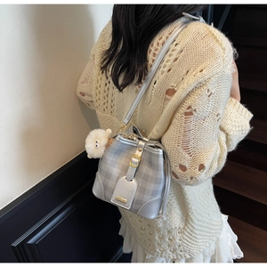 Detail of silver-gray plaid bucket bag with a plush lamb pendant on a model's shoulder