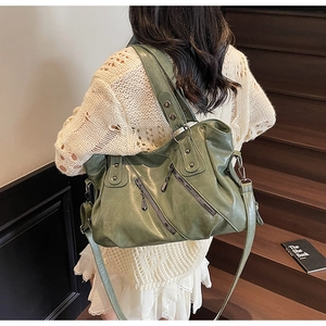 Dettaglio borsa a tracolla in pelle verde scuro con cerniere diagonali e manici rinforzati