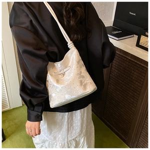 Detail of white bucket bag with silver butterfly texture and elegant pearl bow pendant