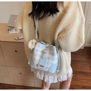 Detail of light blue plaid bucket bag with plush lion charm and metal nameplate decoration