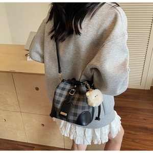 Detail view of checkered bucket bag with leather trim and plush ball pendant charm