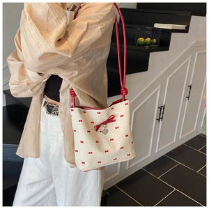 Detail view of cream bucket bag with red ribbon prints and a heart charm on a model
