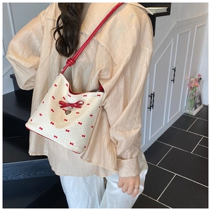 Close-up of cream shoulder bag with red bow patterns and heart pendant detail