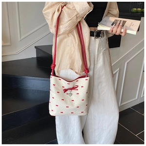 Detail of cream bucket bag with red bow prints and a heart-shaped metal pendant charm