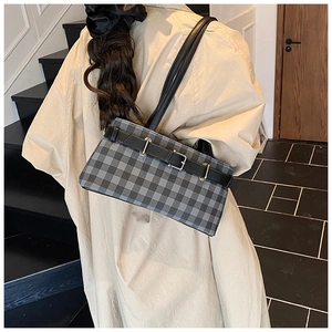 Detail of a plaid underarm bag with black leather straps shown on a shoulder