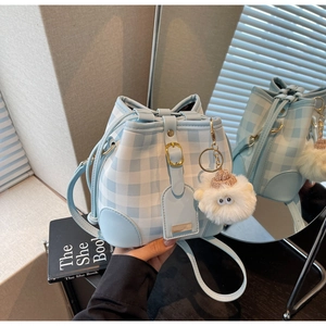 Detail view of a blue and white checkered bucket bag with a cute white plush pendant