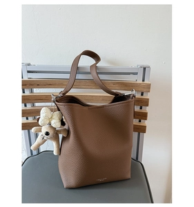 Detail of dark brown lychee leather bucket bag with a cute white puppy plush charm