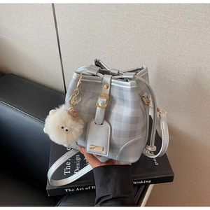 Silver checkered bucket bag with gold hardware and white plush charm on books