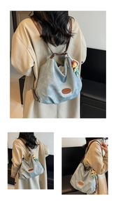 Detail view of a light blue canvas tote bag with brown leather strap and cartoon doll charm