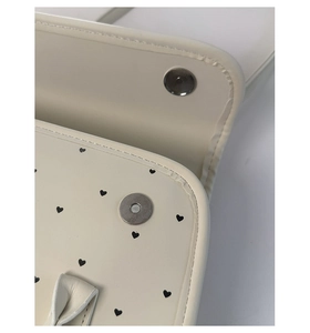 Detail of magnetic snap closure and black heart print on beige leather shoulder bag
